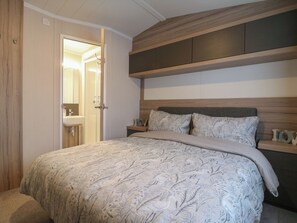 Quarto com cama, mesa de cabeceira, cabeceira de madeira e porta para um banheiro.