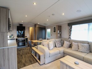 A modern living room with a sofa, a dining table, and a kitchen area with appliances. - No 20 Barley Way (Colchester)