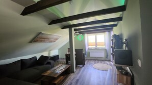 A loft-style living room with a sloped ceiling, a sofa, a coffee table, a TV, and a window with curtains. - Apartment -Sorayas Welt- direkt hinter dem Deich mit allen Annehmlichkeiten (Neufeld)
