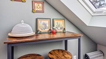 Une pièce avec un plafond en pente, une table sur laquelle se trouve un objet blanc, et deux tableaux encadrés représentant des tournesols.