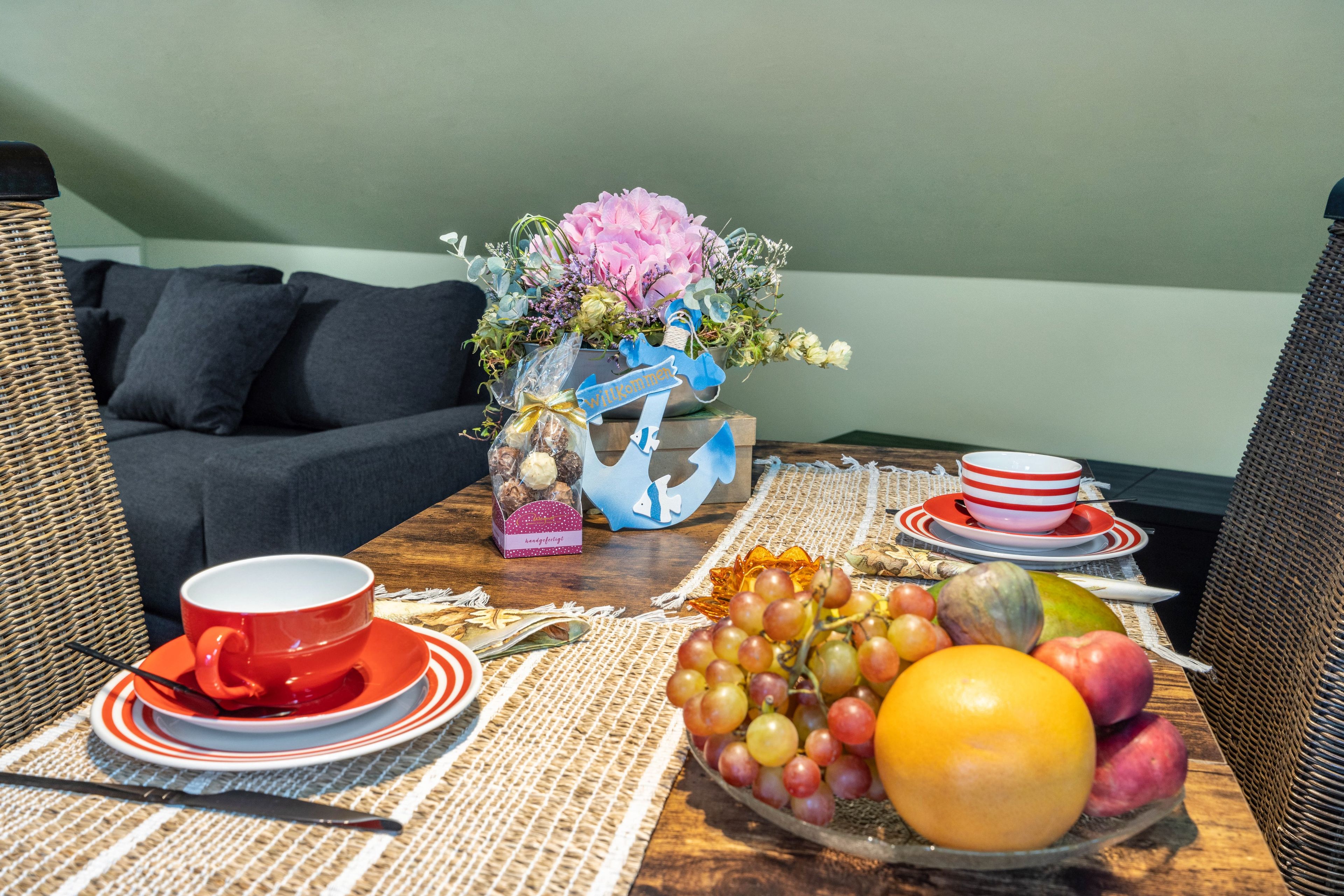 Una mesa de comedor con un frutero, una taza roja y un plato de galletas.
