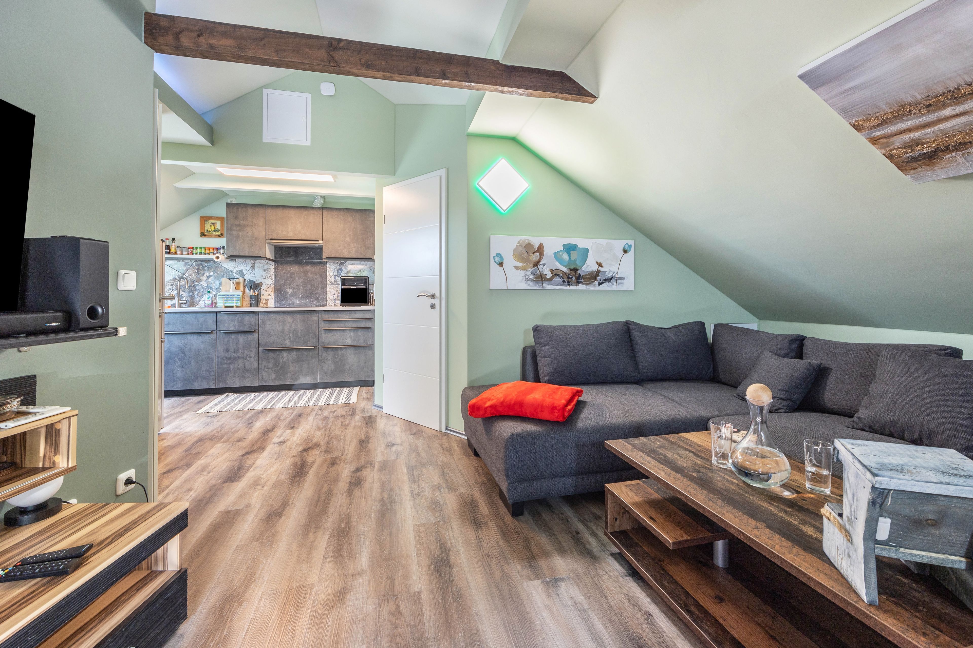 Una sala moderna con un sofá gris, una mesa de centro de madera y una cocina al fondo.
