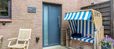 A brick building with a blue door, a wooden chair, and a striped outdoor seating area.