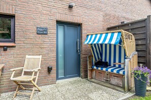 A brick building with a blue door, a wooden chair, and a striped outdoor seating area. - Apartment -Sorayas Welt- direkt hinter dem Deich mit allen Annehmlichkeiten (Neufeld)