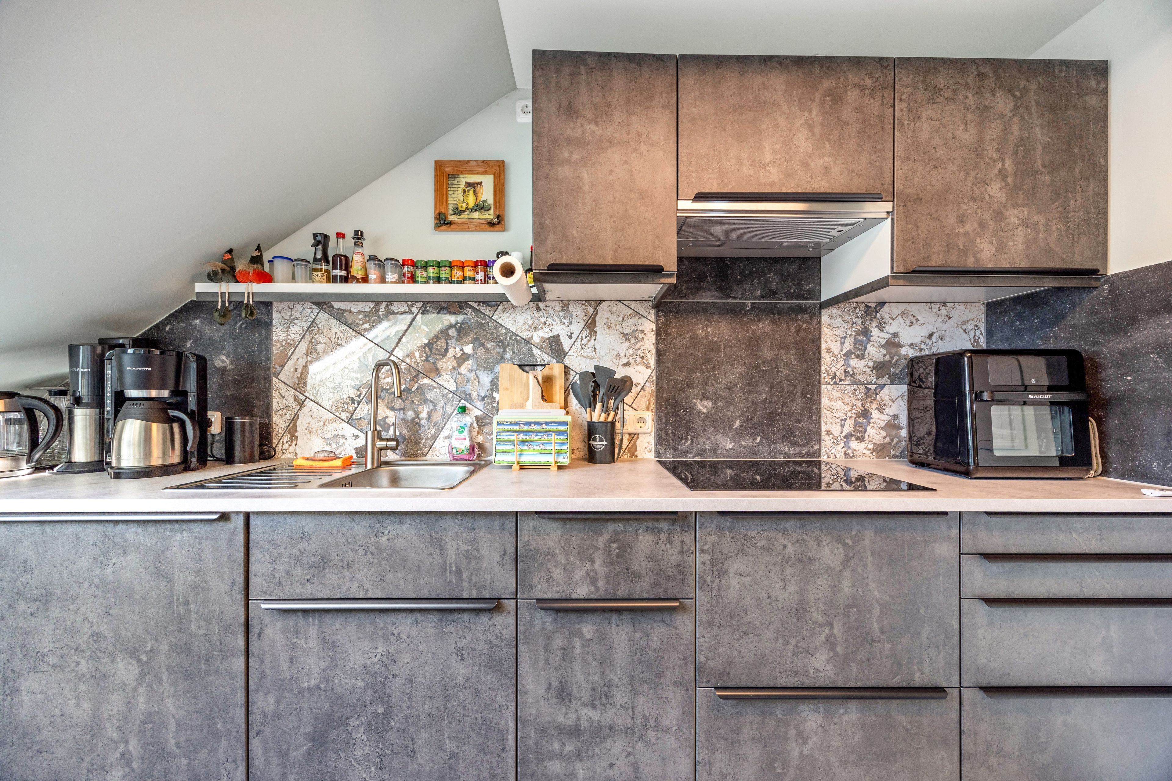 Una cocina moderna con gabinetes oscuros, salpicadero de mármol y electrodomésticos de acero inoxidable.