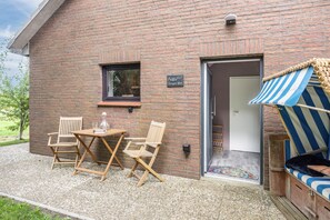 A brick building with a small patio area featuring a table, two chairs, and a striped awning. - Apartment -Sorayas Welt- direkt hinter dem Deich mit allen Annehmlichkeiten (Neufeld)