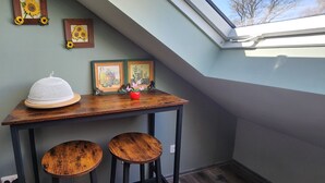 A room with a sloped ceiling, a skylight, a wooden table with two stools, and framed artwork on the wall. - Apartment -Sorayas Welt- direkt hinter dem Deich mit allen Annehmlichkeiten (Neufeld)