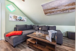 A modern living room with a grey sectional sofa, a wooden coffee table, and a painting on the wall. - Apartment -Sorayas Welt- direkt hinter dem Deich mit allen Annehmlichkeiten (Neufeld)