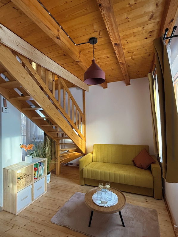 A wooden interior with a staircase, a sofa, a table with glasses, and a bookshelf.