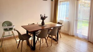 Un'area pranzo con tavolo in legno, sei sedie, una seggiolina bimbo, un vaso con fiori e una finestra con tende.