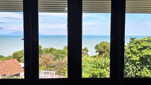 Vista a través de una ventana que muestra un cuerpo de agua, vegetación y una cadena montañosa distante.
