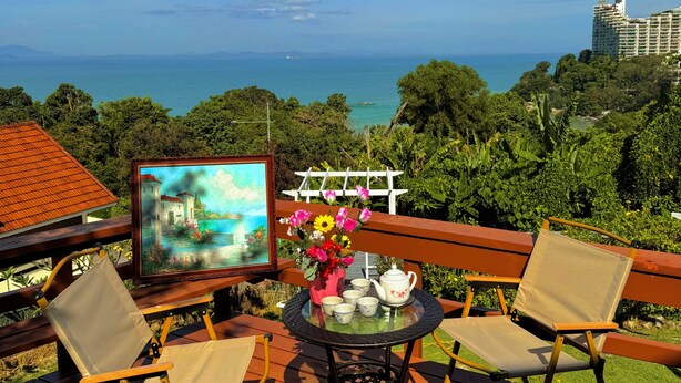 Una terraza con dos sillas, una mesa con tetera y tazas, un cuadro y vistas al océano y edificios.