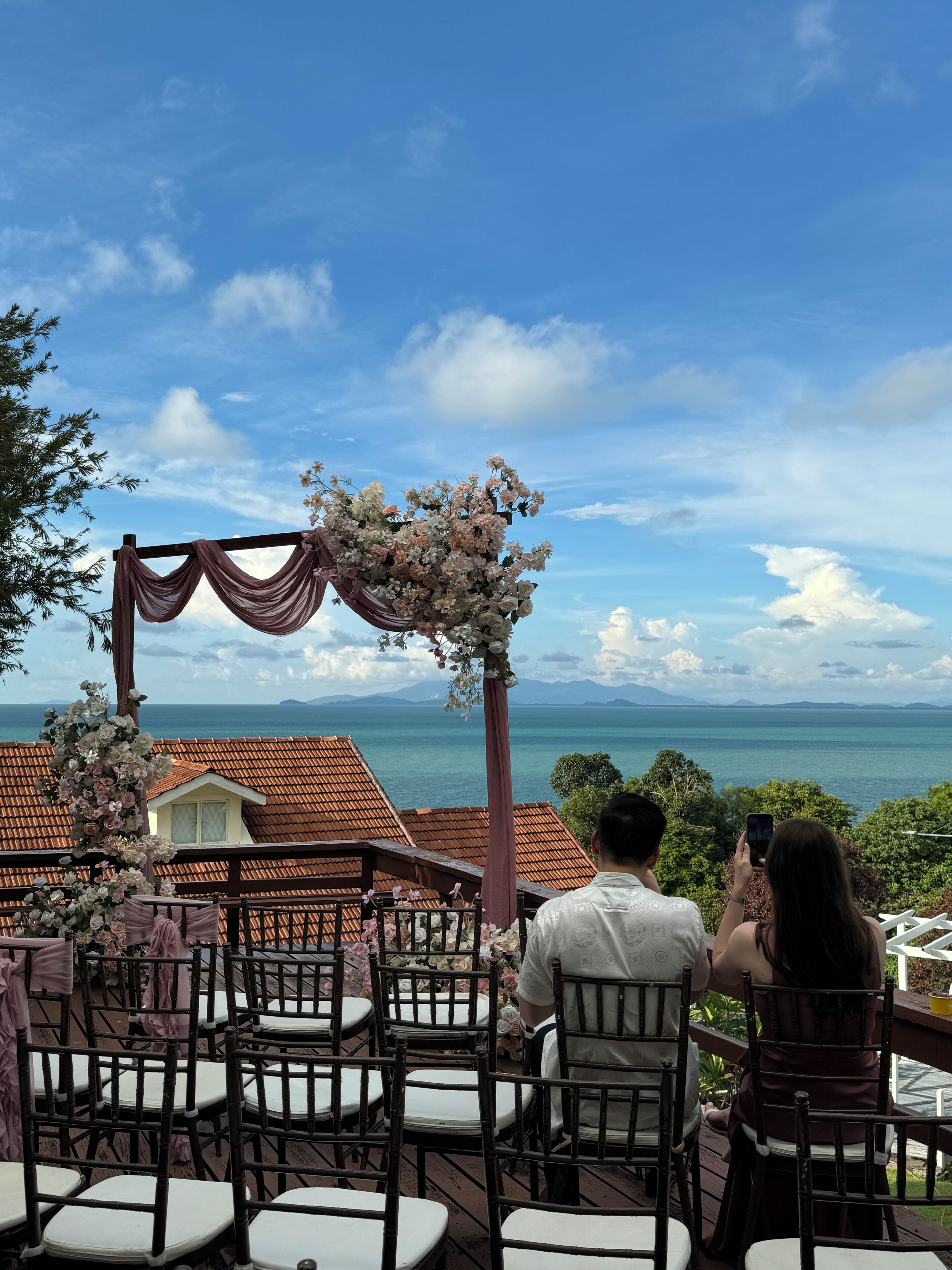 A wedding ceremony setup with chairs and a floral arch, overlooking a scenic ocean view.
