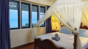 Un dormitorio con cama con dosel, vistas al mar a través de amplios ventanales y una mesita de noche con lámpara.