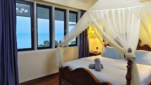 Un dormitorio con cama con dosel, vistas al mar a través de amplios ventanales y una mesita de noche con lámpara.