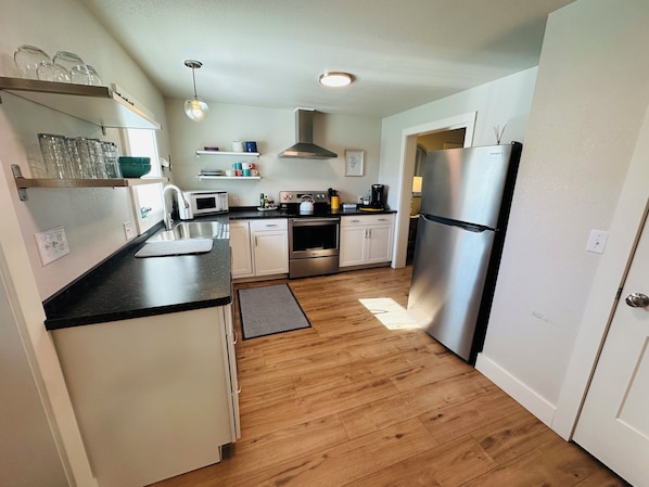 A compact kitchen with white cabinets, a stainless steel refrigerator, a microwave, and a kettle.