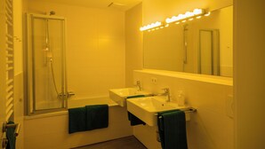 Ett badrum med en dusch som är avskärmad med glasväggar, två handfat, en spegel med belysning och handdukar som hänger på väggen.