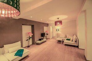 A modern living room with a white sofa, a small white table, a TV, and a pink flower. - Haus Spiegel - Holiday apartment Oriental (Lindau (Bodensee))