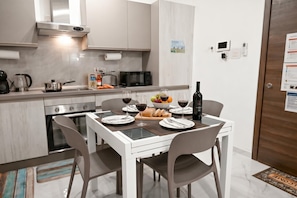 A modern kitchen with a dining area, equipped with a stove, oven, microwave, and a small refrigerator. - Cosy 2bdr Apart In Bugibba Square (St. Paul's Bay)