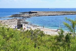 A rocky beach with clear blue water, a lifeguard tower, and some people. - Cosy 2bdr Apart In Bugibba Square (St. Paul's Bay)