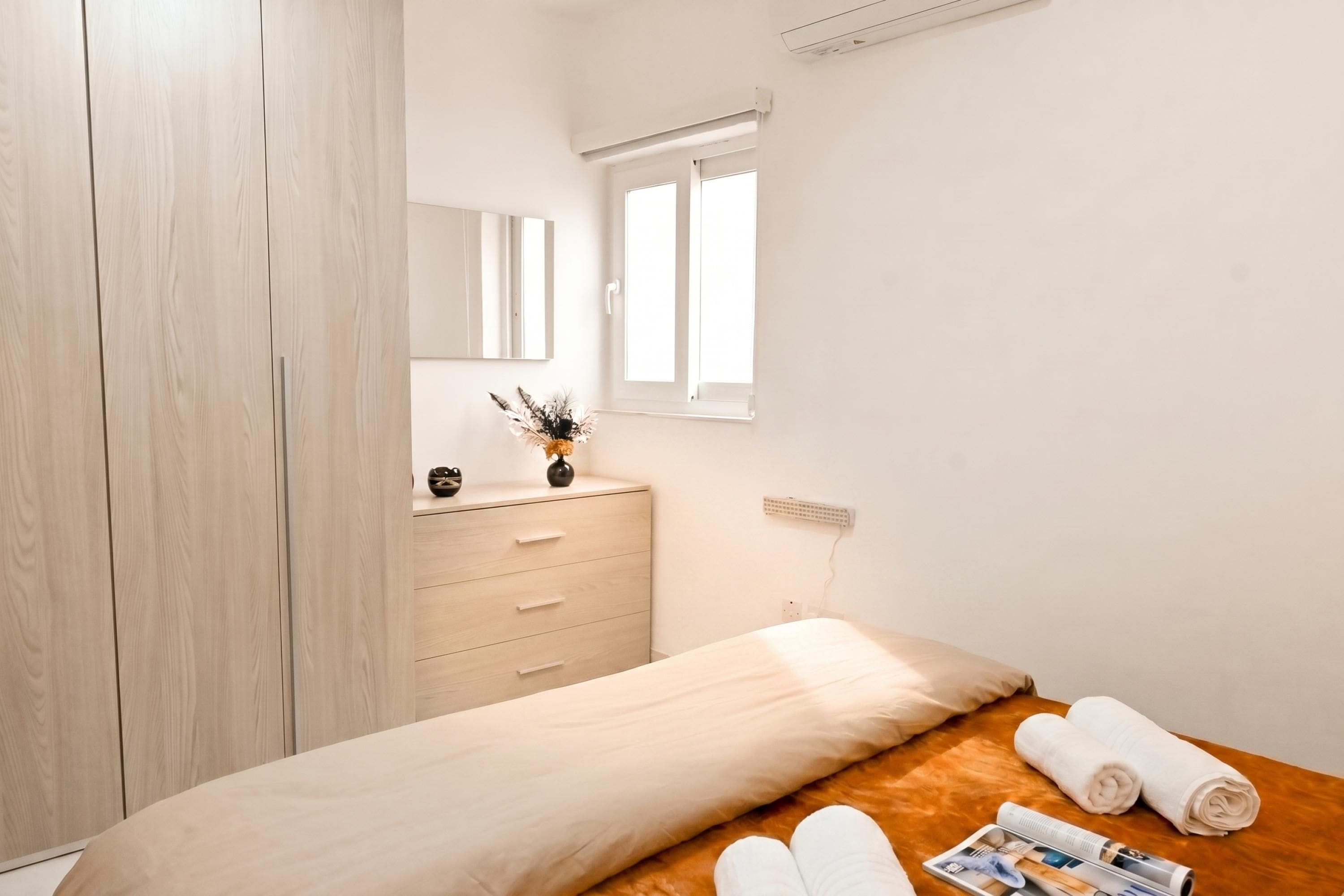 Ein Schlafzimmer mit einem Bett, einem Holzschrank, einem Schminktisch, einem Fenster und einer Steckdose.