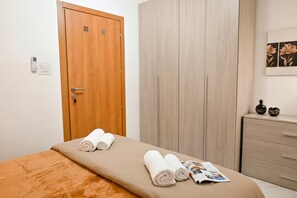 Habitación de hotel con puerta de madera, armario, cama con cubrecama color beige y una revista sobre la cama.