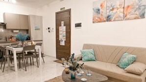 A modern living room with a sofa, coffee table, and dining area. - Cosy 2bdr Apart In Bugibba Square (St. Paul's Bay)
