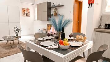 Un comedor con una mesa blanca, sillas grises y un cuenco de fruta.