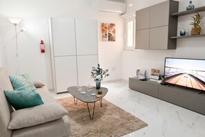 A modern living room with a sofa, coffee table, TV, and a fireplace. - Cozy 2bdr Apart In Bugibba Square (St. Paul's Bay)