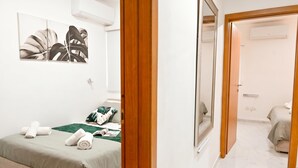 A hotel room with a bed, a green throw, towels, a mirror, and a painting on the wall. - Cosy 2bdr Apart In Bugibba Square (St. Paul's Bay)