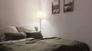 Un dormitorio con cama, lámpara, dos cuadros enmarcados y techo inclinado.