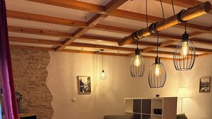 Una sala de estar acogedora con una mesa de madera, un banco y una chimenea. Hay varias luces colgantes y un sofá con cojines.