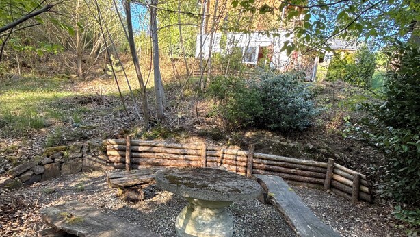 Un espacio al aire libre rústico con un hogar de piedra rodeado de troncos y grava.