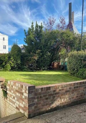 Un muro de ladrillo, una zona cubierta de césped y una estructura alta con un techo puntiagudo.