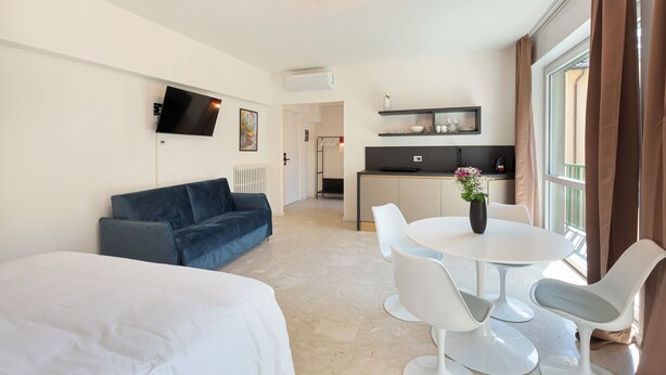 Een moderne hotelkamer met een bed, een slaapbank, een eethoek met tafel en stoelen, een kitchenette en een televisie aan de muur.