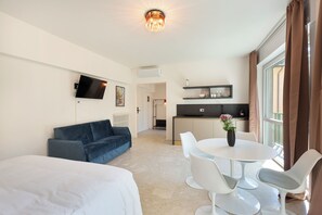A modern hotel room with a bed, a sofa, a dining area with a table and chairs, a kitchen area, and a TV mounted on the wall. - Pharmacy A (Stresa)