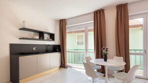 Een moderne keuken met een zwart aanrecht, een witte eettafel met vier stoelen, en een balkon met bruine gordijnen.