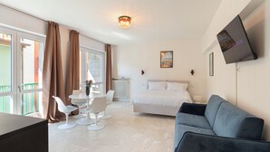 Een hotelkamer met een bed, een televisie, een bank, een eettafel met stoelen en een balkon met gordijnen.