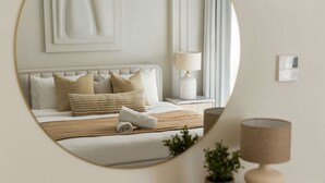 A bedroom with a bed, pillows, a bedside table with a lamp, a mirror, and a wall-mounted artwork. - Silkhaus Polo Residence 1BR 2 Baths Meydan (Dubai)