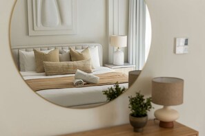 A bedroom with a bed, pillows, a bedside table with a lamp, a mirror, and a wall-mounted artwork. - Silkhaus Polo Residence 1BR 2 Baths Meydan (Dubai)