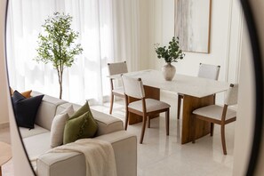 A dining area with a white table, six chairs, a vase with green foliage, and a sofa with cushions. - Silkhaus Polo Residence 1BR 2 Baths Meydan (Dubai)