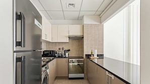 A compact kitchen with a stainless steel refrigerator, a built-in oven, a washing machine, and a microwave. - Silkhaus Polo Residence 1BR 2 Baths Meydan (Dubai)