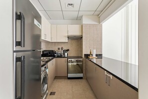 A compact kitchen with a stainless steel refrigerator, a built-in oven, a washing machine, and a microwave. - Silkhaus Polo Residence 1BR 2 Baths Meydan (Dubai)