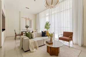 A modern living room with a sofa, armchair, coffee table, and a dining area with a chair and table. - Silkhaus Polo Residence 1BR 2 Baths Meydan (Dubai)