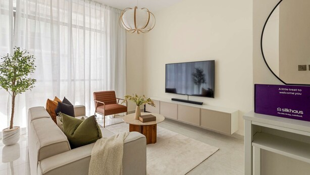 A modern living room with a sofa, armchair, coffee table, and a flat-screen TV. - Silkhaus Polo Residence 1BR 2 Baths Meydan (Dubai)