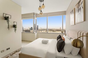 A modern hotel room with a large bed, city view, hanging plants, and a unique ceiling light fixture. - Silkhaus Cityscape 2BR Sky Gardens Difc Centre (Dubai)