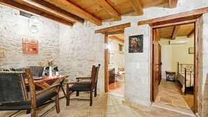 A stone-walled room with a wooden ceiling, a dining table with chairs, and a bed in the adjacent room. - Villa Poseidon - Superior Suite In Zante w Pool (Zakynthos)