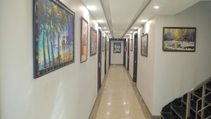 A hallway with artwork on the walls, a staircase on the right, and a polished floor. - The Royal Casa Hotel And Banquet (Ghaziabad)
