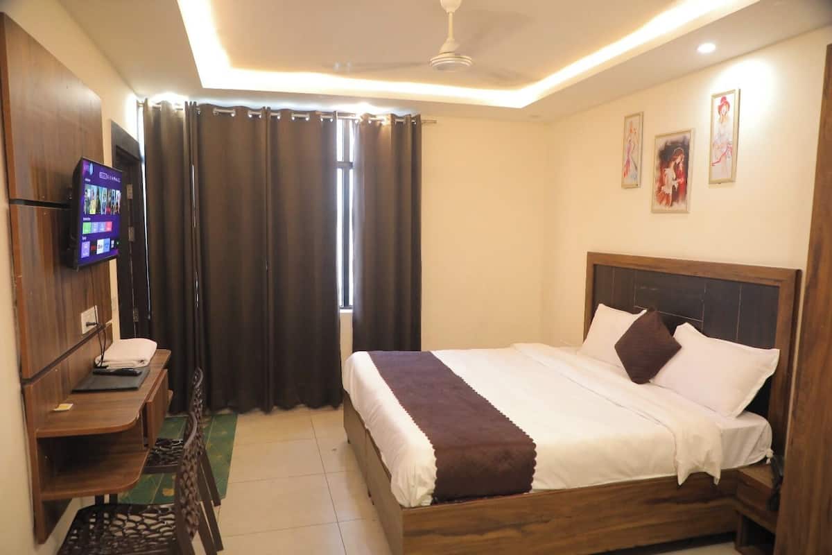 Une chambre d’hôtel comprenant un lit, un bureau avec un téléviseur à écran plat, une chaise et une fenêtre avec des rideaux.