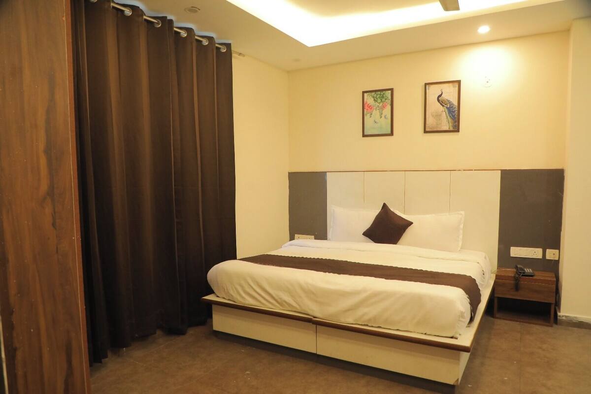 Une chambre d’hôtel avec un lit, des rideaux, une table de chevet, un téléphone et deux tableaux accrochés au mur.